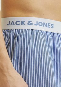 Boxer shorts rayés bleu et blanc avec une ceinture élastique blanche portant le texte "JACK & JONES" en bleu clair. Tissu texturé.
