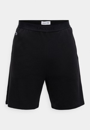 Sorte shortser med strukturert stoff, elastisk midjebånd med 'LACOSTE' logo, og enkelt design. Ingen lommer synlige.