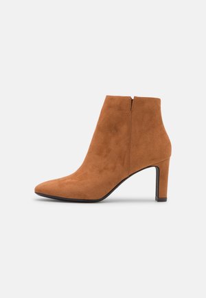 Hnědé semišové kotníkové boty s špičatou špičkou, vysokým stiletto podpatkem a detailem na zadním zipu. Hladká textura s elegantním, moderním designem.