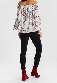 Bílá halenka s odhalenými rameny a růžovým květinovým potiskem, rukávy s volánky; v kombinaci s těsnými černými džíny a červenými sametovými kotníkovými botami.