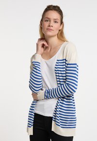 Cardigan a righe in crema e blu, caratterizzato da una texture morbida, apertura frontale, polsini a costine e una silhouette lunga. Indossato sopra una maglietta bianca.