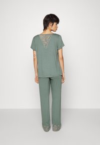 Groen, T-shirt met korte mouwen en kanten driehoekdetail op de rug, gecombineerd met bijpassende groene broek met decoratieve rand aan de zoom.