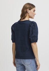 T-shirt marine à manches courtes et bouffantes en tissu brodé. Dos uni, coupe décontractée et col rond. Style décontracté.