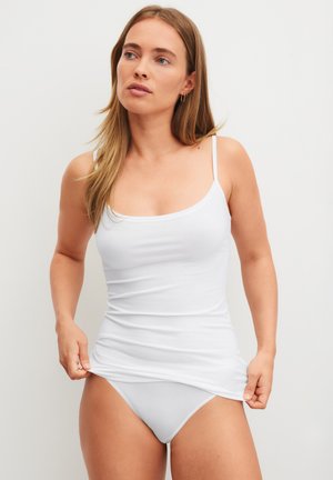 Débardeur en coton blanc à fines bretelles, coupe ajustée et texture lisse, associé à des sous-vêtements blancs assortis.