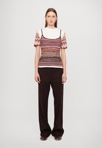 Top tricotat cu dungi, cu mâneci scurte, având modele orizontale multicolore. Asortat cu pantaloni largi de culoare maro închis, cu textură zigzag.