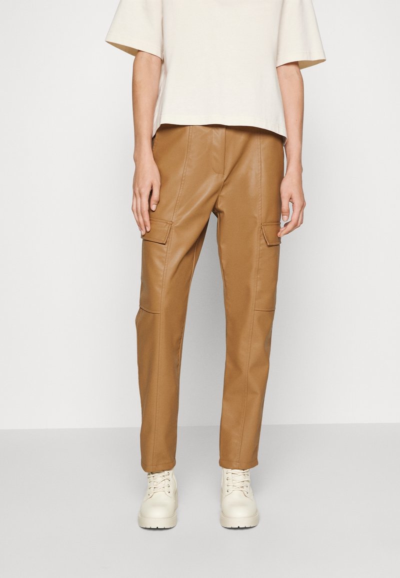 Braune Kunstleder-Cargohosen mit zwei vorderen Taschen, schmalem Schnitt und gestickten Details, kombiniert mit off-white Schuhen.