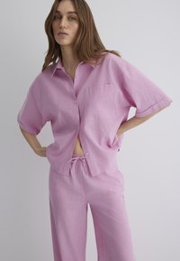 Pink striped short-sleeve shirt with a pocket, paired with matching loose-fit pants. Lightweight fabric with a relaxed design.