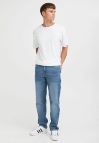 Camiseta blanca de manga corta, jeans azul claro y zapatillas blancas con rayas negras. El ajuste es casual; el denim tiene una textura desgastada.