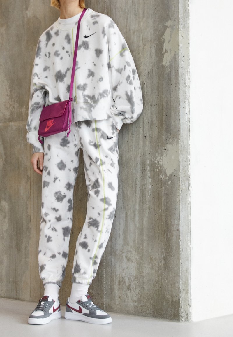 Vit och grå tie-dye sweatshirt och joggers med gröna accenter, tillsammans med grå och vita sneakers och en klar rosa crossbody-väska.