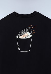 Ψηφιακό ρολόι που εμφανίζει τη λέξη "ΚΟΥΡΑΣΜΕΝΟΣ" με κουμπί "ΑΝΑΒΟΛΗ", το οποίο πετάγεται σε κάδο απορριμμάτων στην πλάτη μαύρου πουκαμίσου.