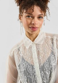 Witte kanten blouse met knopen, met een transparante afwerking, voorzien van een klassieke kraag en bloemenpatronen, aangevuld met doorzichtige mouwen.
