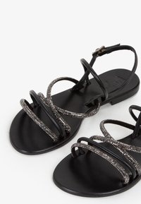 Zwarte platte sandalen met meerdere sprankelende zilveren banden, platte zolen en een slanke enkelgesp. Gladde textuur en open ontwerp voor ademend vermogen.
