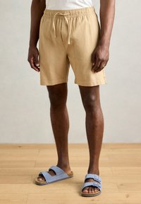 Khaki shorts med elastisk talje og snor. Lavet af tekstureret stof, har de sidelommer og en afslappet pasform. Sammen med blå sandaler.