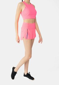 Conjunto de sujetador deportivo y falda rosa con un diseño recortado, aberturas laterales y detalles perforados, combinado con zapatillas deportivas negras.