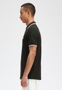 Polo nero con colletto e polsini bianchi a contrasto, maniche corte e logo ricamato sul petto. Tessuto dalla consistenza liscia.