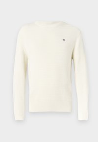 Kerma-vaalea neulepusero, jossa on teksturoitu neuloskuvio, resorireunukset hihoissa ja helmassa sekä pieni logodetaili rinnassa. Pitkät hihat, pyöreä kaula-aukko.