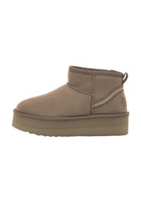 Stivaletti in suede marrone, con punta rotonda, cuciture minime e suola piatta in gomma. Presentano una piccola linguetta sul retro per facilitare l'indossamento.