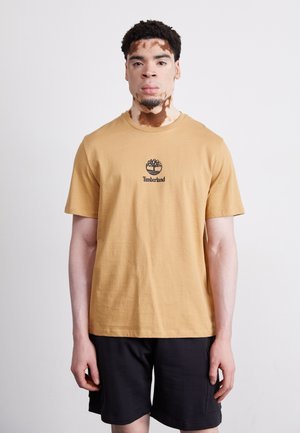 T-shirt en coton jaune moutarde avec un logo Timberland noir sur la poitrine, associé à un short noir. Design simple et épuré.