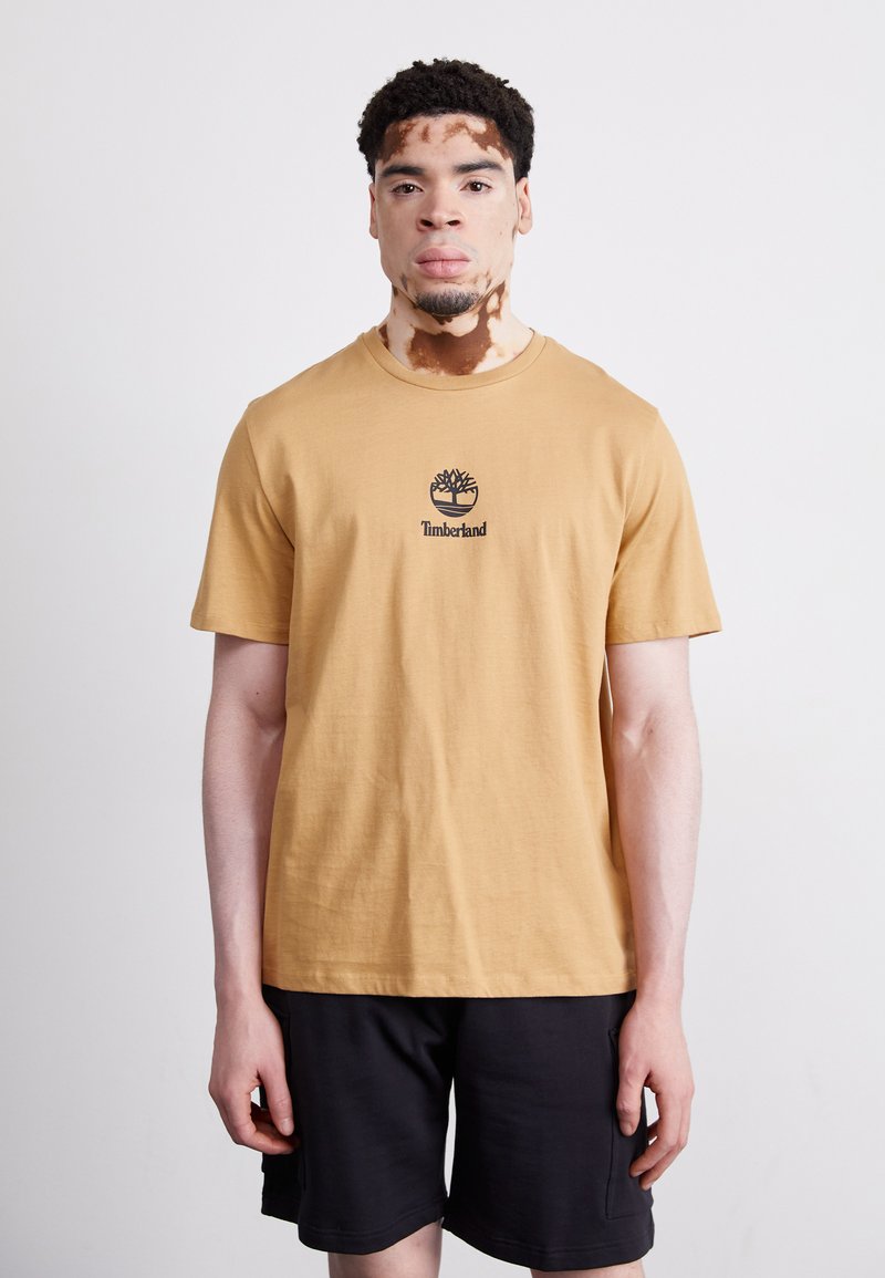 Sennepsgul bomulls T-skjorte med en svart Timberland-logo på brystet, sammen med svarte shorts. Enkelt, uten dekorasjoner.