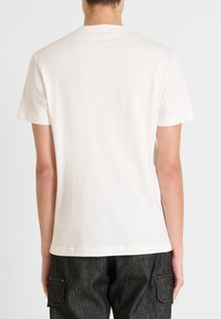 Camiseta blanca de algodón con mangas cortas y cuello redondo. Textura suave, sin patrones visibles ni logotipos en la parte de atrás.