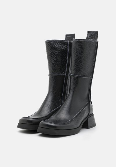 Botas de tornozelo em couro preto com um acabamento texturizado, costura branca, ponta quadrada e um salto robusto. Concebidas com fecho de zip no lado.