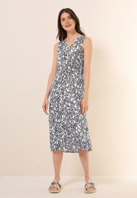 Ärmelloses, knielanges Kleid in Weiß mit schwarzem abstraktem Muster. Verfügt über einen V-Ausschnitt und ein gerafftes Taillendesign. Getragen mit metallischen Sandalen.