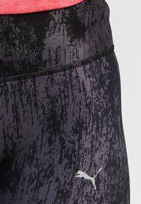Legginsy w czarno-fioletowy wzór z teksturowanym materiałem, z wysokim stanem i białym logo Pumy na dolnej części nogawki.