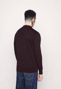 Ciemnofioletowy sweter z długim rękawem i okrągłym dekoltem. Miękka faktura i prążkowane mankiety, noszony z niebieskimi dżinsami. Prosty, dopasowany fason.