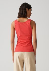 Top a canotta rosso, aderente, realizzato in morbido cotone, con scollatura rotonda e spalline larghe, abbinato a pantaloni a vita alta color beige chiaro.