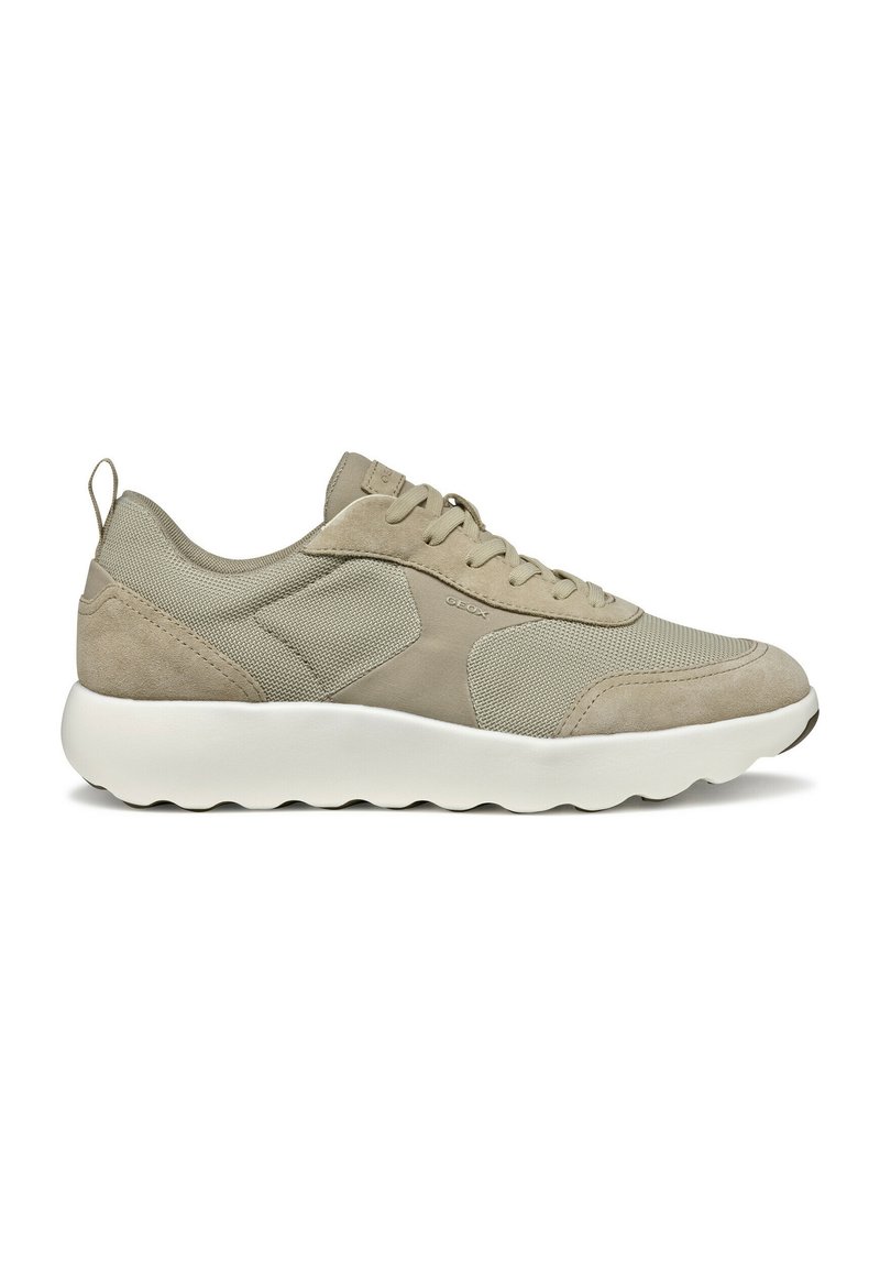 Scarpa sportiva beige con materiali in rete e suede, suola bianca arrotondata e allacciatura frontale. Presenta un branding discreto e un risvolto sul tallone.