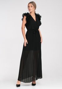 Schwarzes Maxikleid mit plissiertem Rock, V-Ausschnitt, Rüschensäumen und einem gebundenen Taillendetail. Weicher, leichter Stoff mit transparenter Schichtung.
