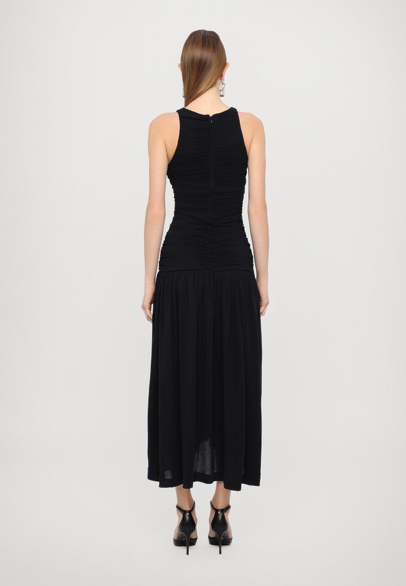 Schwarzes ärmelloses Kleid mit geraffter Textur am Oberteil, fließendem Rock und einem Reißverschluss auf der Rückseite. Getragen mit schwarzen Sandalen mit Absatz.