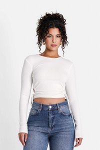 Top crop bianco a maniche lunghe in tessuto a coste con lacci laterali; abbinato a jeans in denim blu a vita alta. Design liscio e aderente.