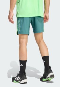 Turquoise shorts hebben een ademende textuur en een groen "CLIMACOOL" logo. Zwarte sokken met witte strepen en sportieve schoenen maken de look compleet.