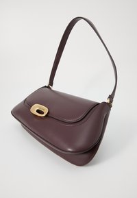 Sac à main en cuir bordeaux avec un fermoir en métal doré, design incurvé, bandoulière réglable et texture lisse.