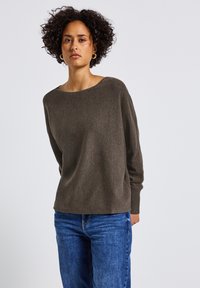 Maglione morbido di cotone marrone scuro con scollo ampio e maniche lunghe, abbinato a jeans blu. Design semplice con vestibilità rilassata.