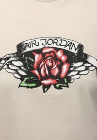 Off-White T-Shirt mit einem grafischen Design einer roten Rose mit grünen Blättern, flankiert von Flügeln und einem Band mit der Aufschrift "AIR JORDAN."