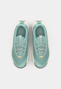Baskets de trail Nike teal avec une tige en mesh, semelles en caoutchouc et accents beiges. Présentent un design texturé et des lacets réfléchissants.