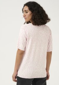 Pull court à manches courtes rose clair avec un motif animal subtil, col rond et poignets côtelés. Texture douce, coupe décontractée.