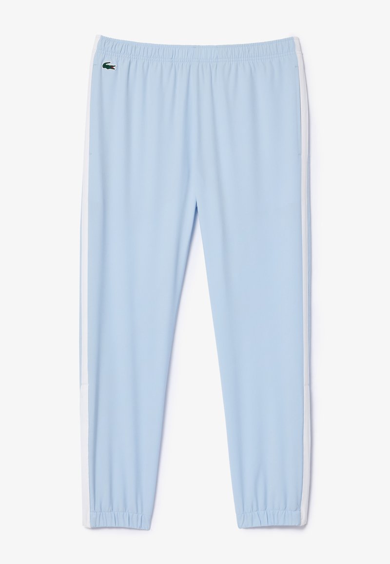 Pantalon de sport bleu clair en tissu lisse, avec une bande latérale blanche et une taille élastique. Logo Lacoste sur la hanche.