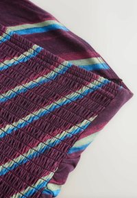 Gros plan sur un tissu violet avec un smock élastique et des rayures diagonales en bleu, beige et marron sur un fond clair.