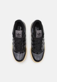 Sapatilhas de verniz preto com design de três riscas, colarinho almofadado e sola de borracha de gengibre. Apresentam fecho com cordões e detalhes texturizados.
