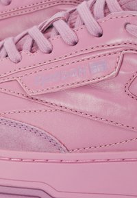 Pink leather sneakers with textured suede accents, featuring matching laces and stitched detailing. Logo tag displayed on the side.