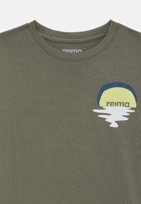 Camiseta verde oliva con textura acanalada, que presenta un diseño gráfico de sol y agua en amarillo y azul en el lado izquierdo del pecho. Nombre de la marca "reima" visible.