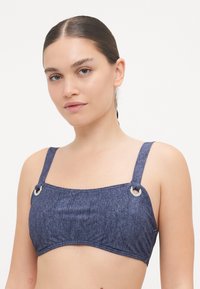 Sötétkék farmer stílusú bikini felső széles pántokkal, ezüstszínű hardver részletekkel és strukturált, téglalap alakú formával.