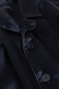 Černá saténová košile s klasickým límečkem, zapínáním na knoflíky s hladkou texturou a jemným leskem. Viditelné dva tmavé knoflíky.