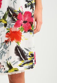 Vestido floral con vibrantes patrones en rojo, rosa y verde sobre un fondo blanco, con un dobladillo texturizado y un borde decorativo de encaje.