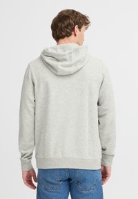 Sudadera gris con capucha ajustable, puños y cintura acanalados, combinada con jeans de mezclilla azul. La tela parece suave y texturizada.