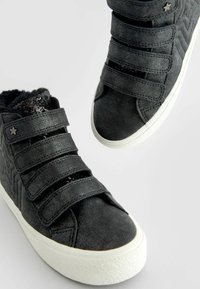 Scarpe alte nere con tre cinturini in velcro, tomaia testurizzata e suola in gomma bianca, caratterizzate da un accento a forma di stella e un morbido rivestimento interno.