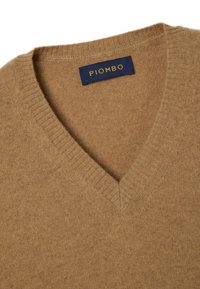 V-Ausschnitt Pullover in warmem Karamellton, hergestellt aus weichem Material mit gerippten Rändern. Das Etikett trägt den Schriftzug "PIOMBO" in Blau mit goldenen Buchstaben.